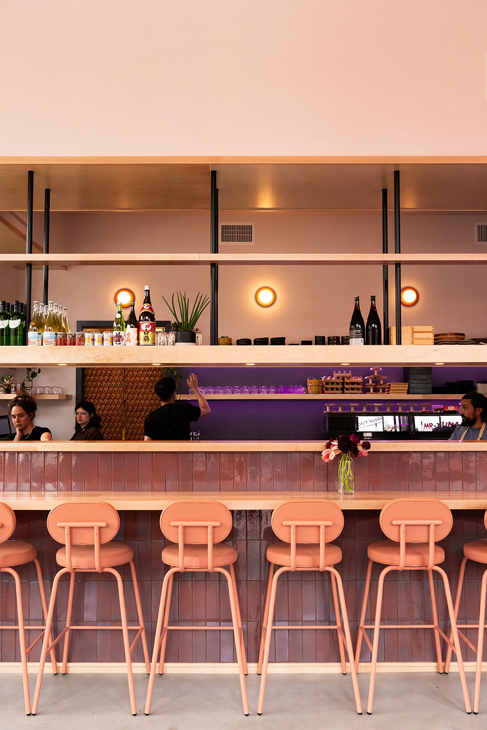 Mey & Co.'s interior design for Mr. Tuna in Portland, Maine, includes a custom sushi bar with terracotta-toned tile, maple shelves, and integrated ambient lighting. The open shelving highlights Japanese sake bottles and curated tableware, reinforcing